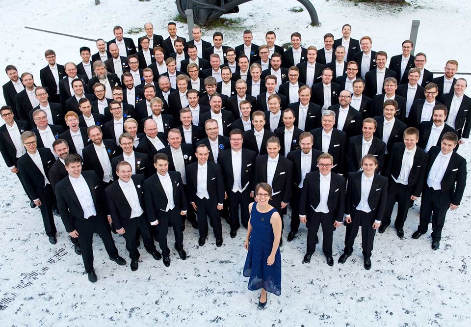 fotografi taget från ovan. Kören står tillsammans med ledare i konsertklädsel. utomhus.