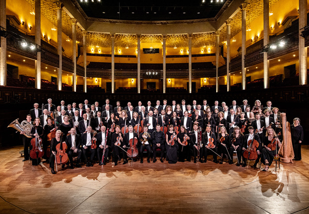 Gruppbild på Kungliga Filharmonikerna inne på podiet i Stora salen. Fotografi.