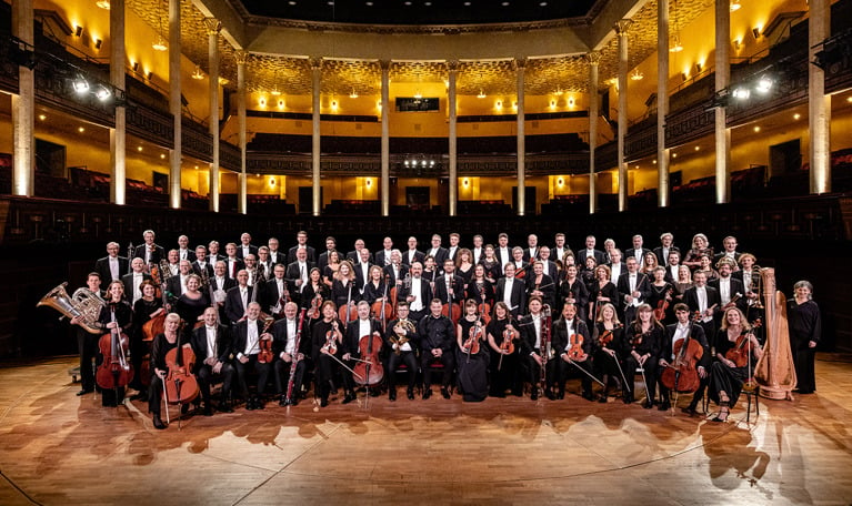 Gruppbild på Kungliga Filharmonikerna inne på podiet i Stora salen. Fotografi.