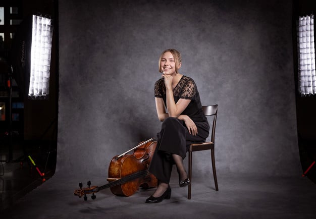 Porträttbild på en leende kvinna med cello. Fotografi.