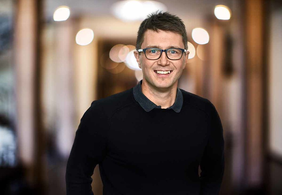 Kristofer Öberg ser glad ut, ler och ser in i kameran. Porträttfotografi.