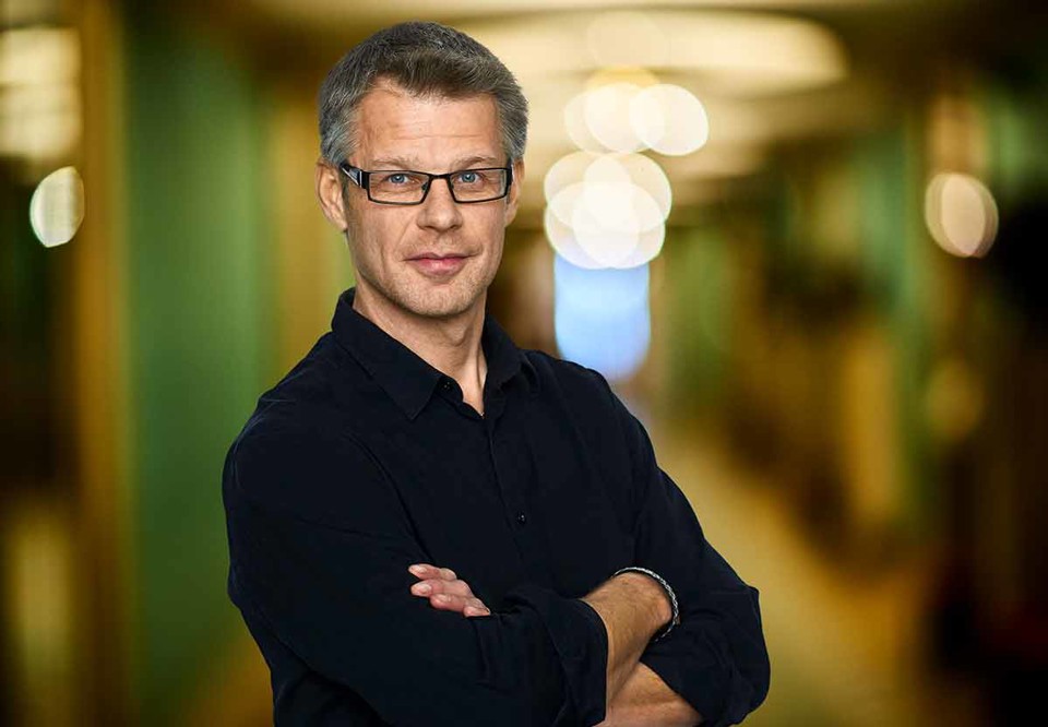 Jesper har händerna i kors men ser glad ut. Porträttbild. Fotografi.