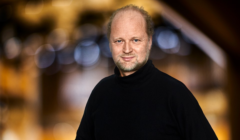 Man i svart tröja står i stora salen. Porträttfotografi.