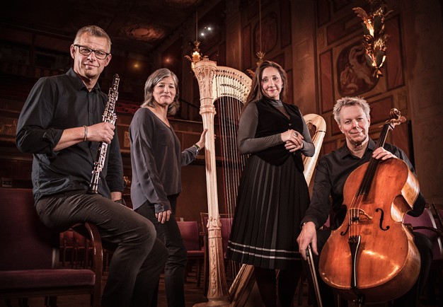 Fyra musiker som står och sitter med sina instrument. Fotografi.