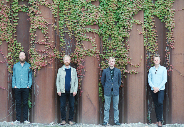 Fyra personer som står mot en vägg. Fotografi.