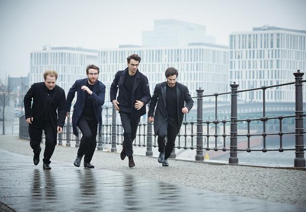 Fyra personer i svarta kläder springer fram i stadsmiljö. Foto.