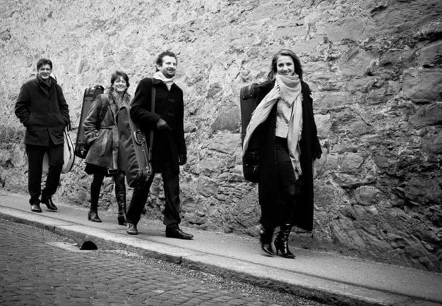 Gruppbild på kvartetten, de går utomhus på en väg, ledigt klädda. Glada. Svartvitt fotografi.
