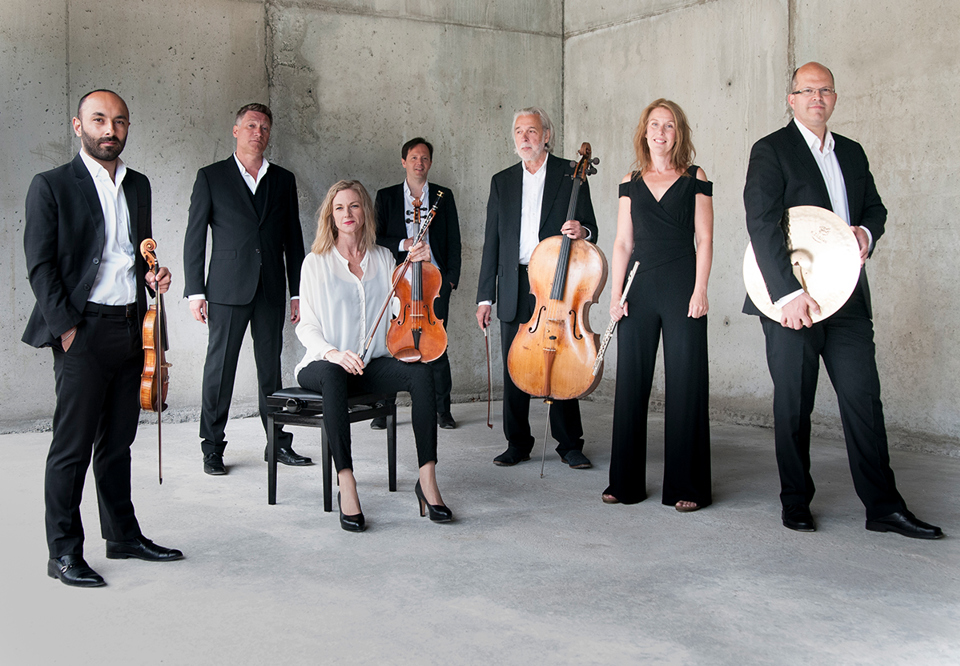 Group image of concert-dressed musicians in the background a concrete wall.