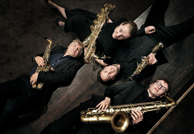 Fyra musiker som håller i sina instrument. Fotografi.