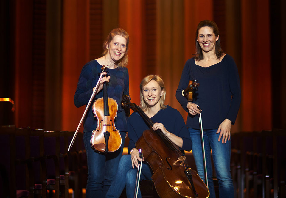 Tre kvinnor som står framför scenen i Grunewaldsalen. Fotografi.