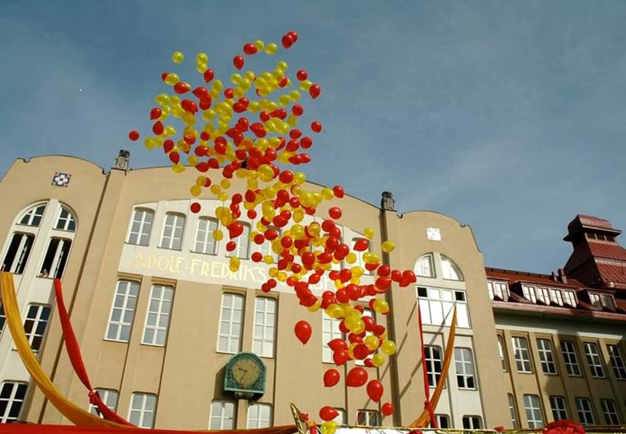 Fotografi på en skolbyggnad. Ballonger i olika färger flyger förbi. Foto.