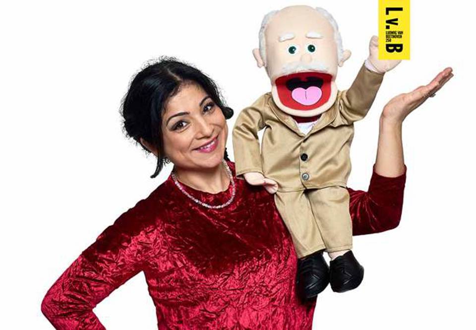 Woman with dark hair and red dress. A doll depicting Ludwig van Beethoven sits on his shoulder.