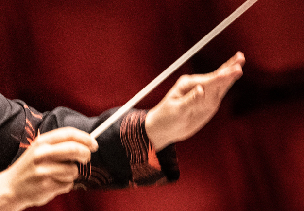 Fotografi på dirigentens händer, med en dirigentpinne i ena handen. 