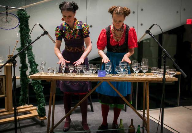 Two women standing behind a table, playing on glasses. Photo.