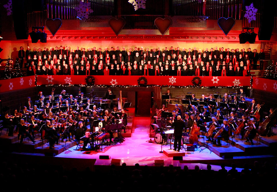 Upplyst scen med rött ljus och granar och stor orkester. Fotografi.