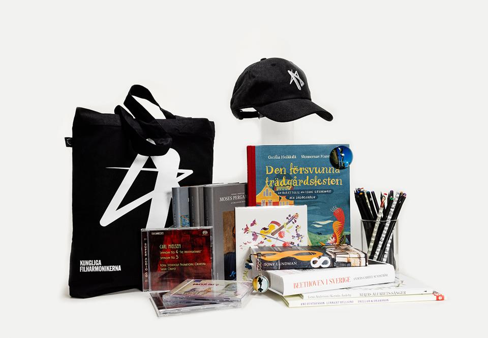 Different items from the shop - a black textile bag, CDs, books and a black cap. Photo.