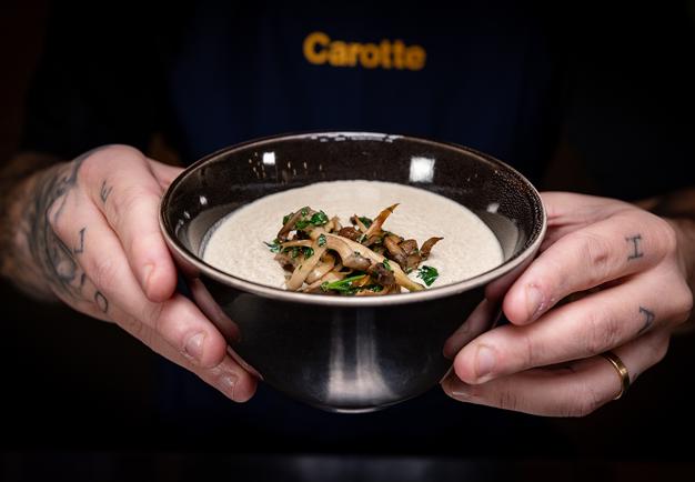 Soup in a bowl topped with mushrooms, hold by two hands. Photo.