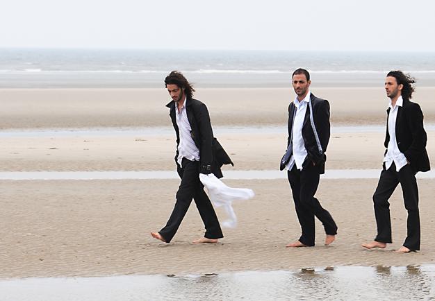 Tre män på en strand. Fotografi.