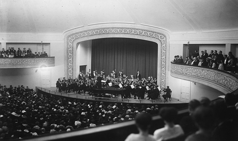 En stor, rund sal med vitmålade väggar. Äldre fotografi inifrån Auditorium vid Norra Bantorget, orkesterns hemvist innan Konserthuset stod klart 1926.