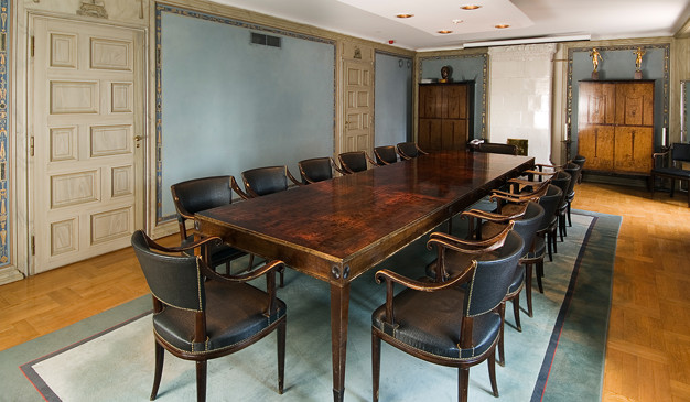 Large table on a blue carpet. Heavy chairs around it. Photo.