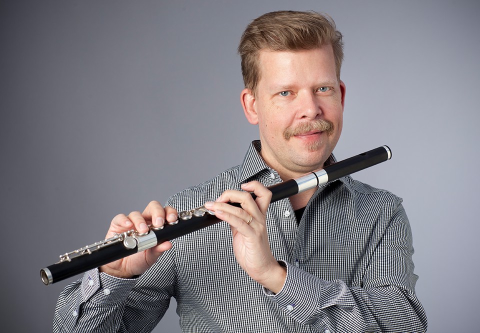 Anders står med sin flöjt, ser glad ut. Fotografi.
