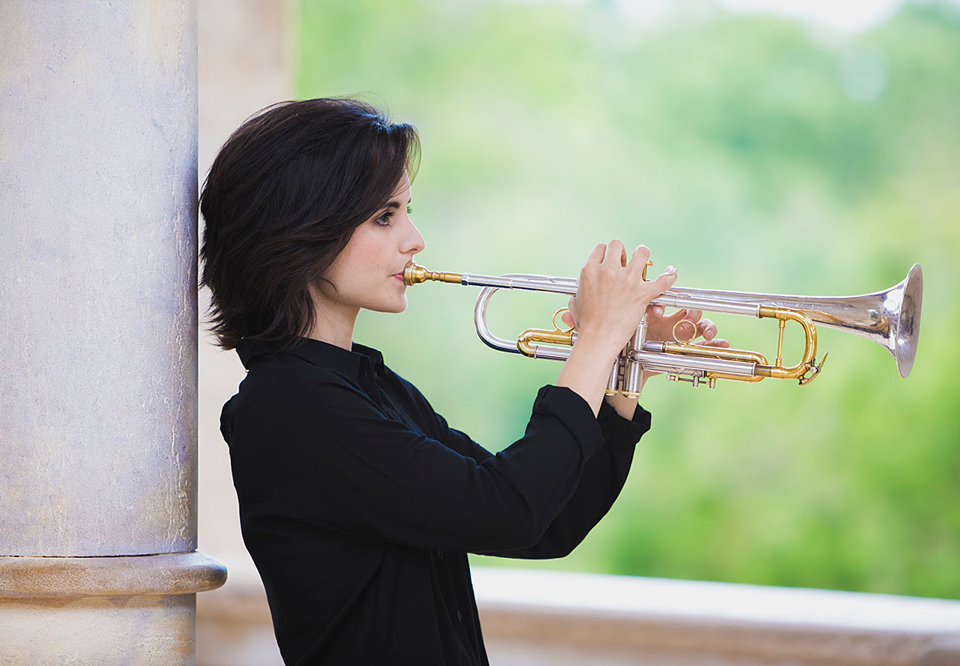 Ung mörkhårig kvinna som spelar trumpet. Fotografi.