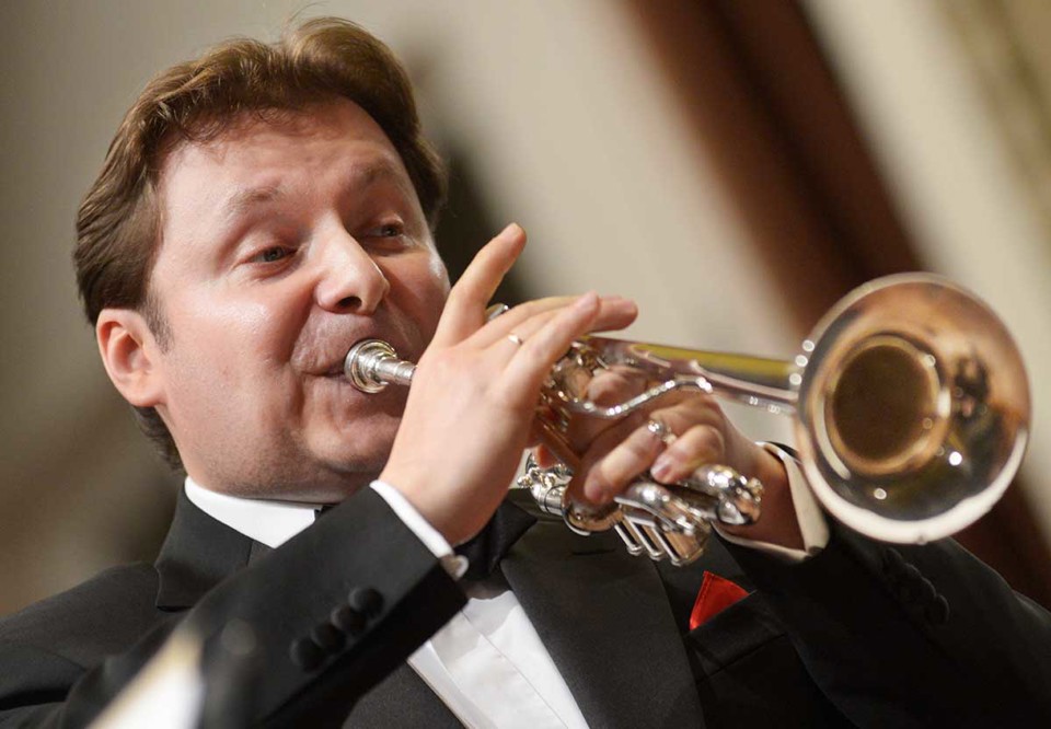 Man uppklädd i frack som blåser i sin trumpet. Fotografi.