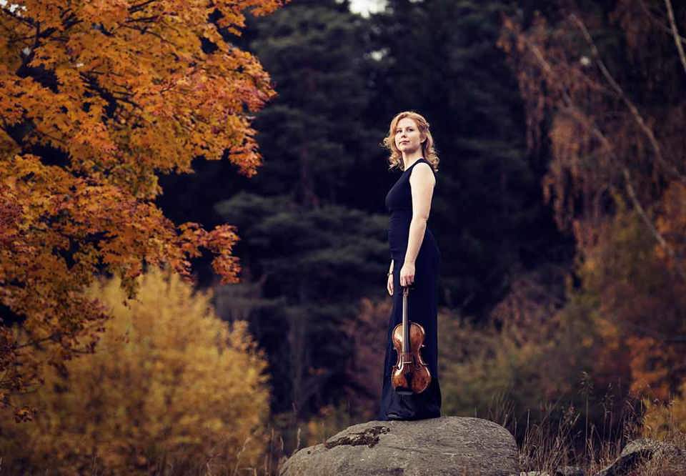 Young woman standing on a cliff with her violin. Photo.