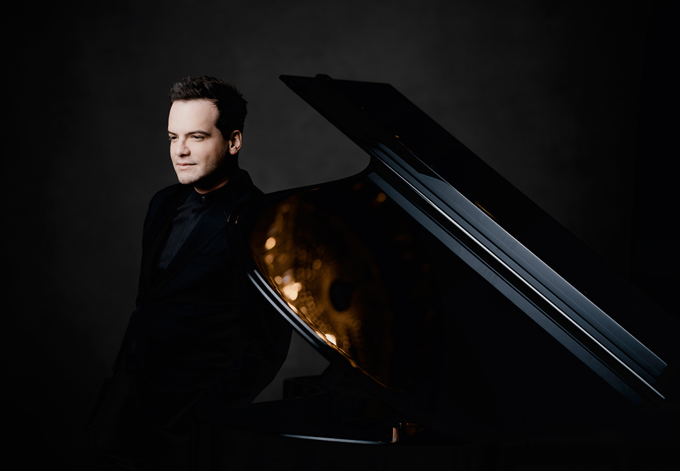 Man standing beside a piano. Photo.