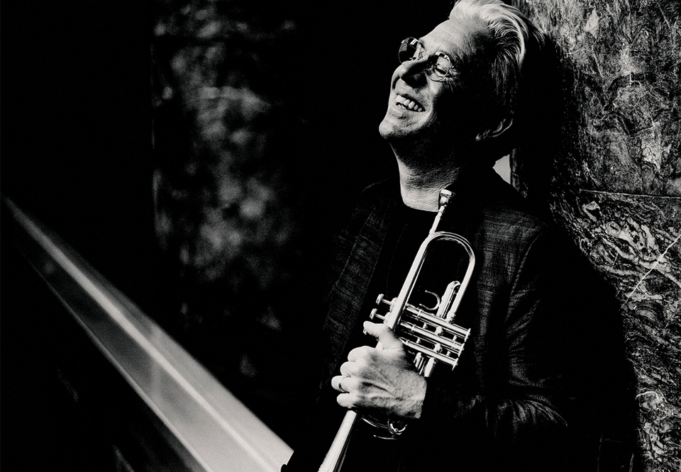 Man with his trumpet leaning to a tree. Photo.