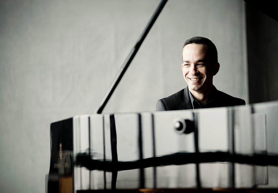 Inon sits at his grand piano, black and white photography.