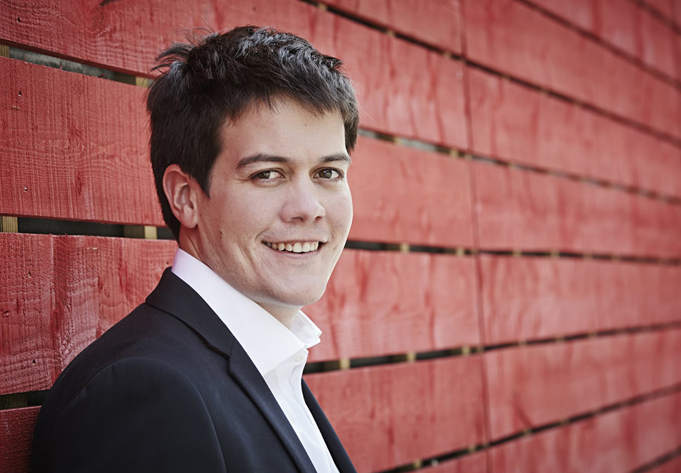 Young man standing agaist a red wall. Photo.