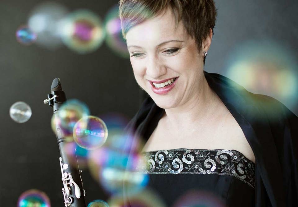 Karin står och ser glad ut med hennes klarinett. Uppklädd i festkläder med såpbubblor flygandes runt. Fotografi.
