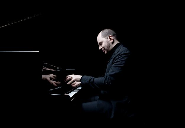 Pollini is sitting by his piano. Black and white photo.