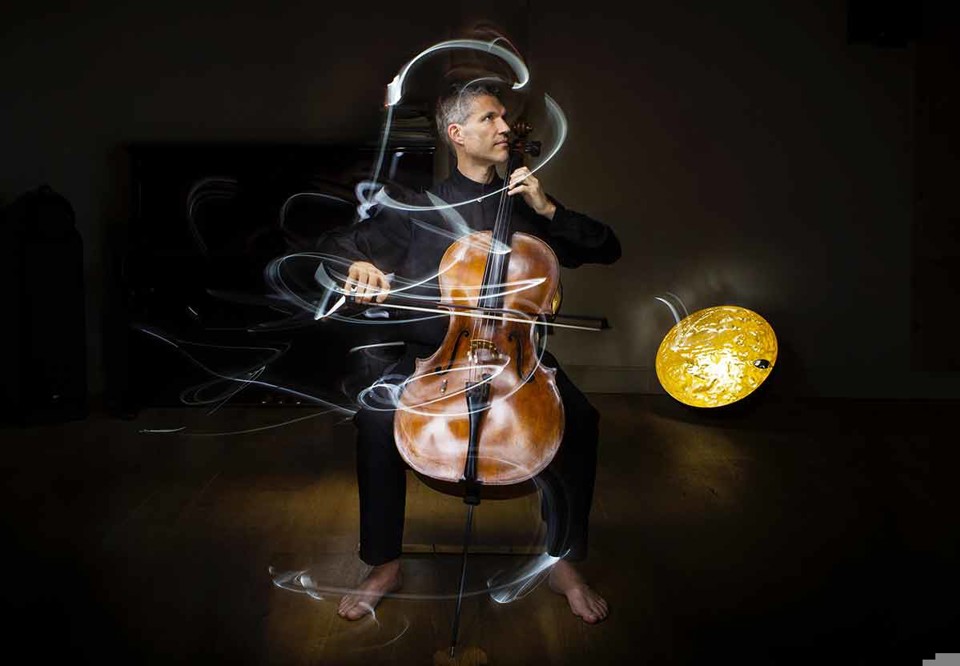 Matthew spelar på sin cello, konstnärlig bild där stråkens rörelser har lämnat färgglada streck efter sig. Fotografi.