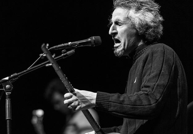 Musician Mohsen Namjoo captured from the side playing his persian lute and singing with lots of expression. Black and white photograph.