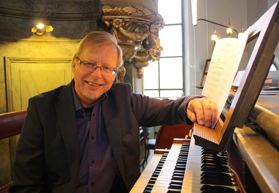 Ralph sitter vid sin orgel. Ser glad. Fotografi.