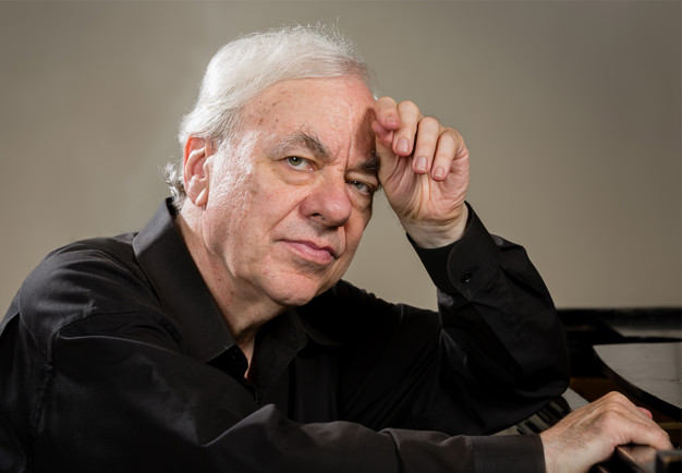 Fundersam pianist lutandes mot svart flygel. Richard Goode. Fotografi.