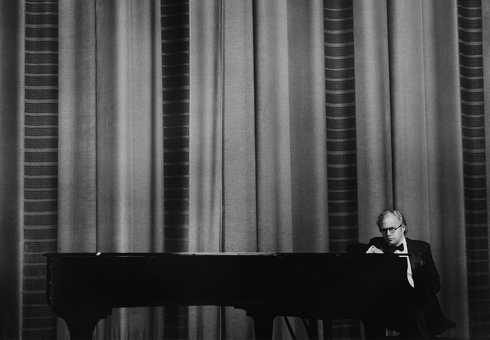 Svart vitt foto med man som sitter vid ett piano. Fotografi.
