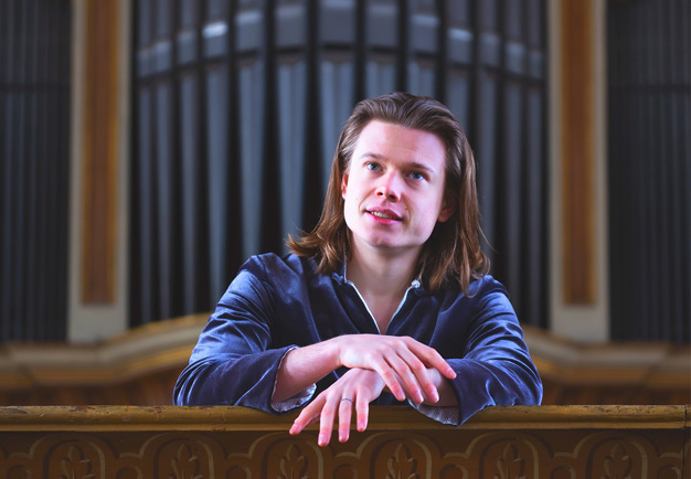 Man som sitter framför en orgel. Fotografi.