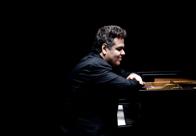 Man against dark background sitting at a grand piano. Photography.