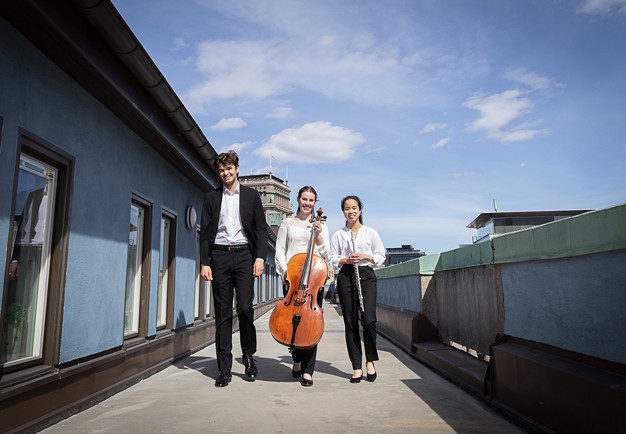Tre musiker som går med sina instrument. Fotografi.