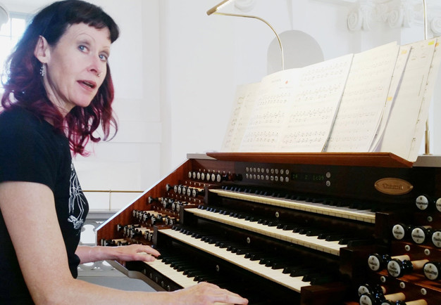 Närbild påkvinna med långt hår vid en orgel. Fotografi.