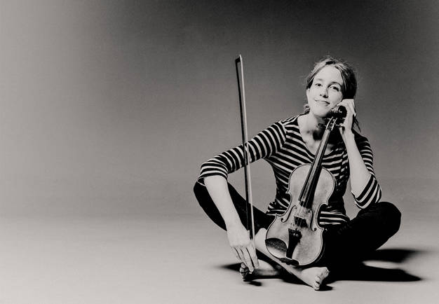 Kvinna som sitter på golvert med sin fiol. Fotografi.