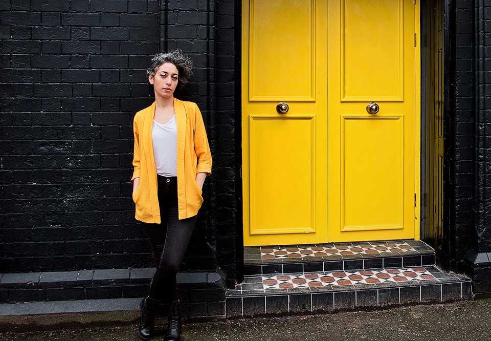 Kvinna som står vid gula dörrar. Fotografi.