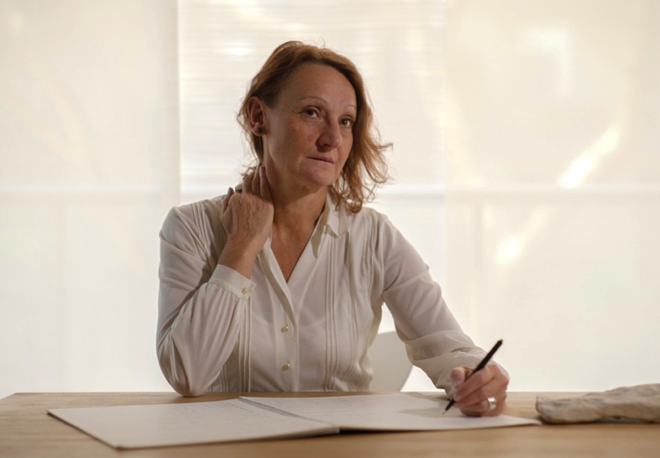 En kvinna i vit blus, Marie Samuelsson, sitter och skriver vid sitt skrivbord. Fotografi.