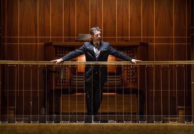 Man stående mot räcket fram en orgel. Fotografi.